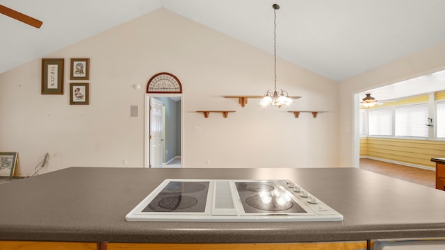 kitchen featuring hardwood / wood-style flooring, ceiling fan with notable chandelier, white stovetop, lofted ceiling, and pendant lighting