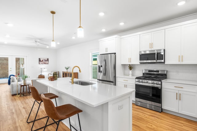 kitchen with white cabinetry, stainless steel appliances, light hardwood / wood-style flooring, an island with sink, and pendant lighting