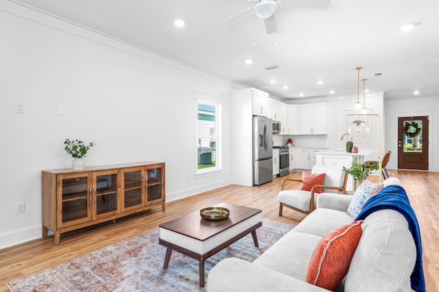 living room featuring light wood-type flooring, ceiling fan, crown molding, and sink