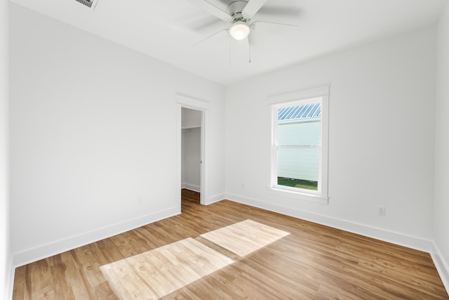 unfurnished bedroom featuring wood-type flooring, a walk in closet, a closet, and ceiling fan