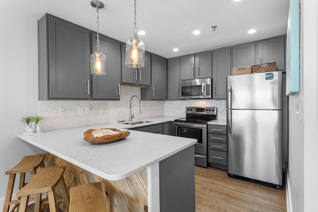 kitchen with kitchen peninsula, a kitchen bar, gray cabinetry, stainless steel appliances, and sink