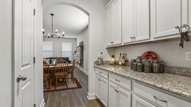 bar with baseboards, arched walkways, dark wood-style floors, an inviting chandelier, and pendant lighting