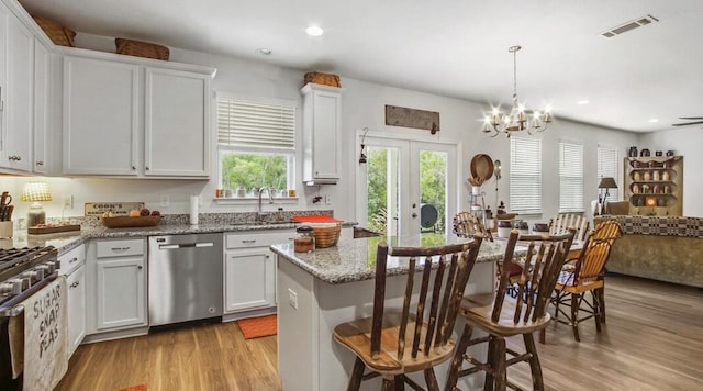 kitchen featuring open floor plan, appliances with stainless steel finishes, light stone counters, and white cabinets