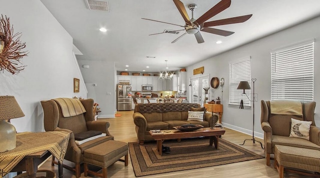 living room with light wood finished floors, recessed lighting, visible vents, baseboards, and ceiling fan with notable chandelier