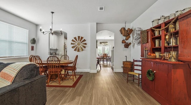 dining area featuring an inviting chandelier, visible vents, arched walkways, and wood finished floors