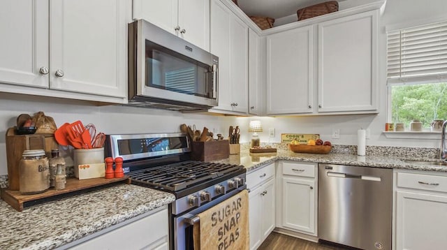 kitchen featuring stainless steel appliances, white cabinets, a sink, and light stone counters