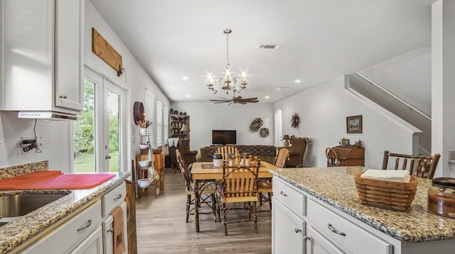 kitchen with pendant lighting, light wood finished floors, visible vents, white cabinetry, and light stone countertops