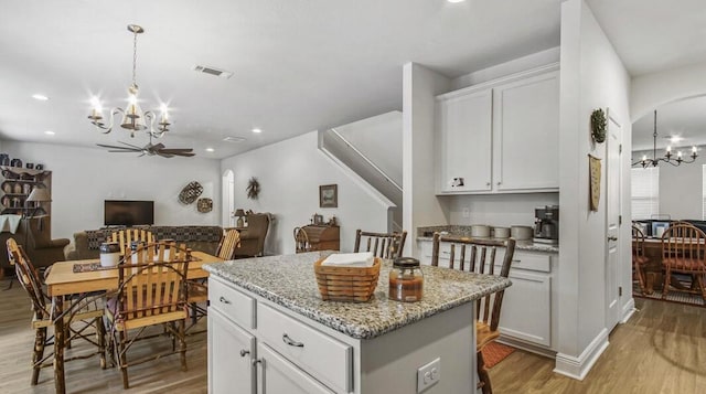 kitchen featuring visible vents, a kitchen island, open floor plan, light stone countertops, and white cabinetry