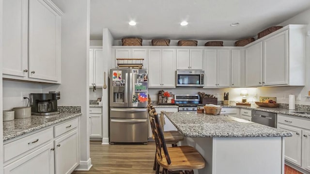 kitchen with light stone counters, stainless steel appliances, a breakfast bar, white cabinets, and a center island