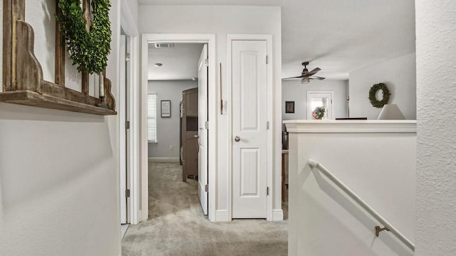 hallway featuring baseboards, visible vents, light colored carpet, an upstairs landing, and a wealth of natural light