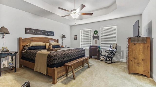 bedroom featuring a ceiling fan, a tray ceiling, light colored carpet, and baseboards