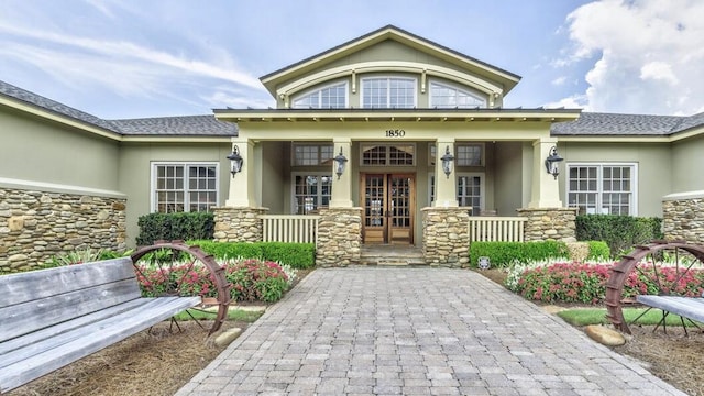 view of front of home with stone siding, covered porch, french doors, and stucco siding