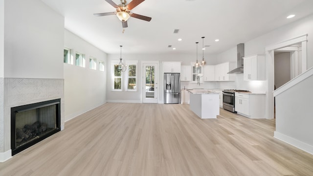 kitchen featuring white cabinetry, hanging light fixtures, stainless steel appliances, a center island, and wall chimney exhaust hood