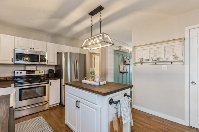 kitchen featuring dark wood-type flooring, white cabinets, a kitchen island, appliances with stainless steel finishes, and decorative light fixtures