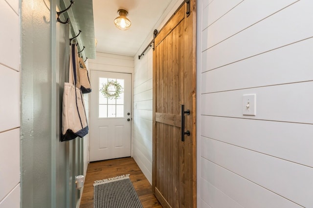 doorway with wood walls, a barn door, and dark hardwood / wood-style floors