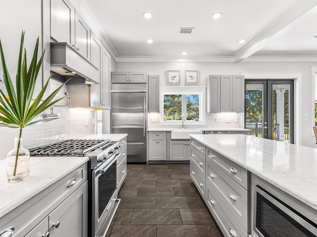 kitchen featuring light stone countertops, built in appliances, gray cabinetry, and sink