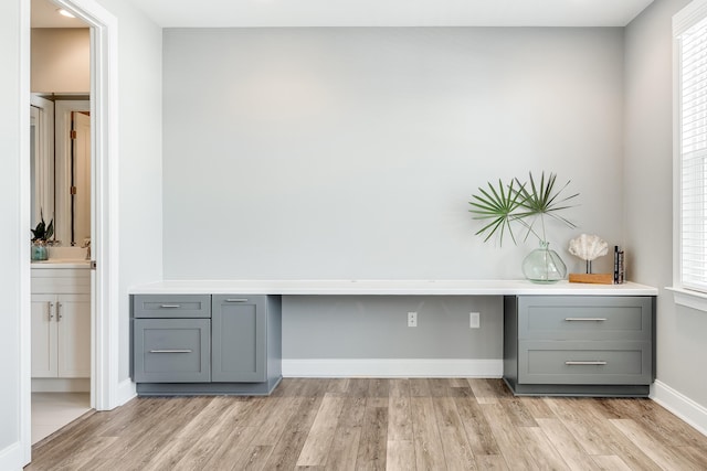 unfurnished office featuring built in desk, light hardwood / wood-style floors, and a healthy amount of sunlight