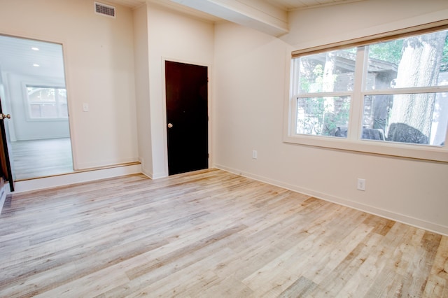 spare room with beamed ceiling and light hardwood / wood-style floors