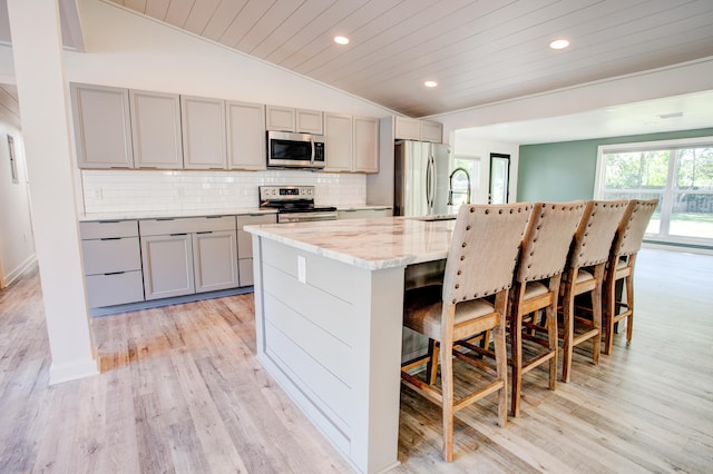 kitchen featuring a breakfast bar area, gray cabinets, vaulted ceiling, and appliances with stainless steel finishes