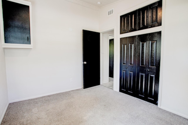 unfurnished bedroom featuring a closet, light colored carpet, and ornamental molding