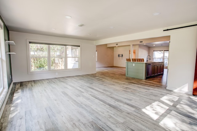 unfurnished living room with a barn door, a wealth of natural light, and light hardwood / wood-style flooring