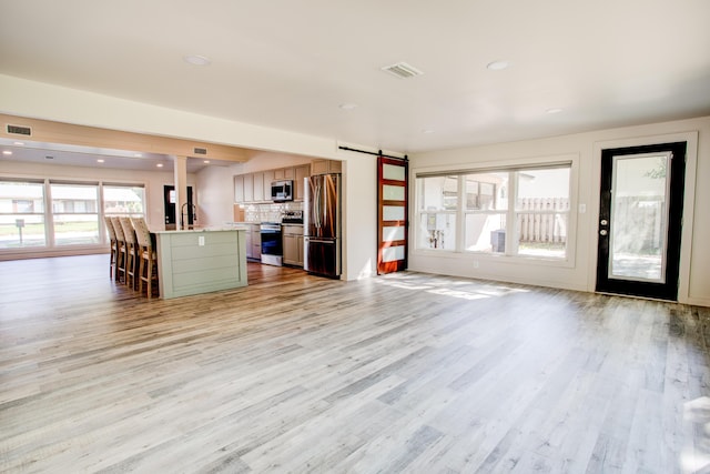 unfurnished living room featuring a barn door, light wood-type flooring, and sink