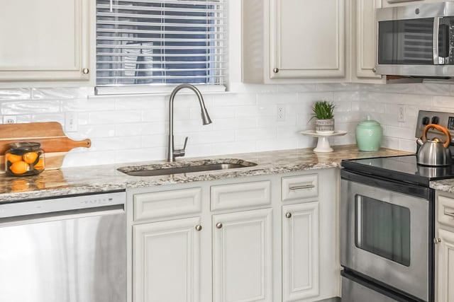 kitchen with light stone countertops, decorative backsplash, appliances with stainless steel finishes, white cabinetry, and a sink