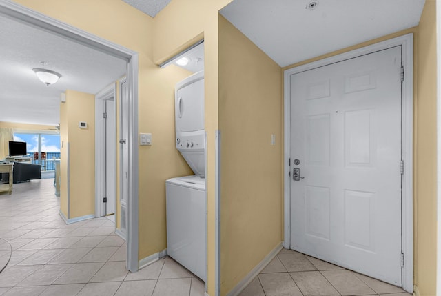 clothes washing area featuring a textured ceiling, light tile patterned floors, and stacked washer and clothes dryer