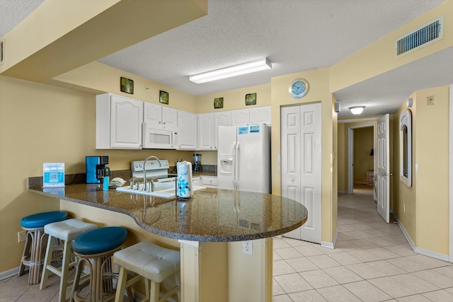 kitchen featuring white cabinets, a kitchen bar, white appliances, and kitchen peninsula