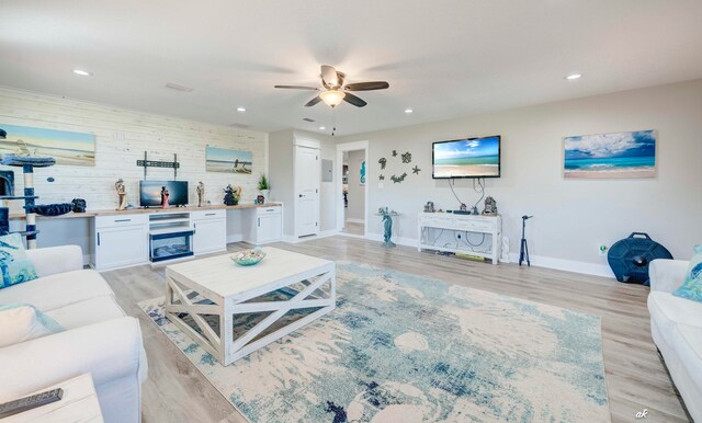 living room featuring ceiling fan, wooden walls, and light hardwood / wood-style floors