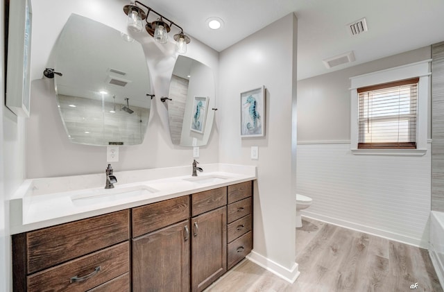 bathroom with tiled shower, toilet, tile walls, hardwood / wood-style floors, and vanity