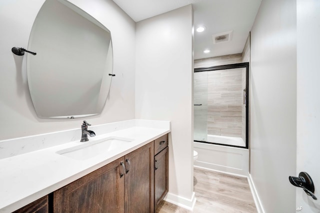 full bathroom featuring hardwood / wood-style floors, shower / bath combination with glass door, toilet, and vanity