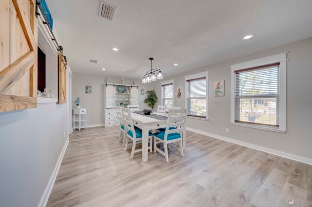 dining area with a barn door, light hardwood / wood-style floors, a chandelier, and a textured ceiling