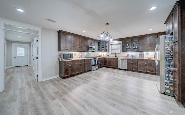 kitchen with appliances with stainless steel finishes, dark brown cabinets, hanging light fixtures, sink, and light hardwood / wood-style flooring