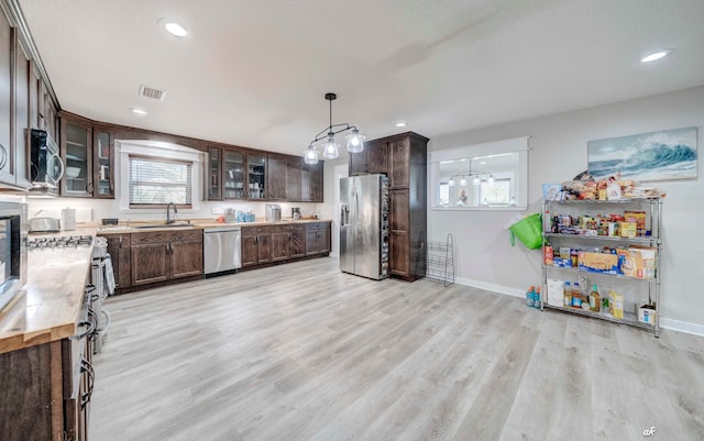 kitchen featuring light wood-type flooring, appliances with stainless steel finishes, dark brown cabinetry, and hanging light fixtures