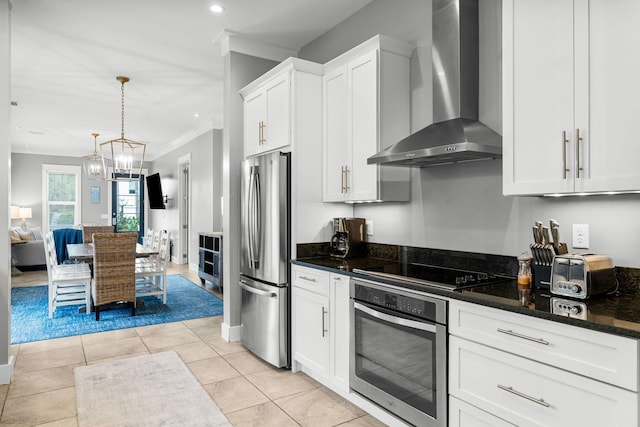 kitchen with light tile patterned flooring, crown molding, white cabinetry, wall chimney range hood, and appliances with stainless steel finishes