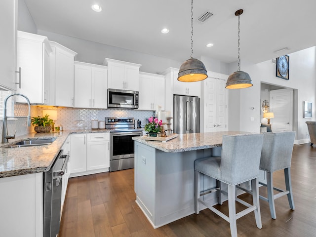 kitchen with sink, appliances with stainless steel finishes, hanging light fixtures, a center island, and white cabinets