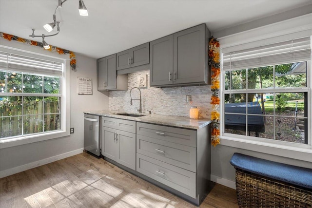 kitchen with dishwasher, sink, gray cabinetry, light stone countertops, and light wood-type flooring