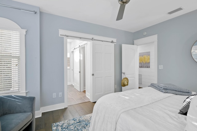 bedroom with hardwood / wood-style floors, ensuite bathroom, ceiling fan, and a barn door