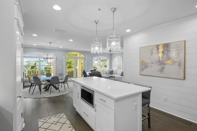 kitchen with white cabinetry, dark hardwood / wood-style floors, pendant lighting, stainless steel microwave, and a center island