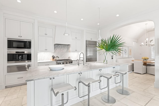 kitchen featuring sink, an island with sink, built in appliances, and white cabinets