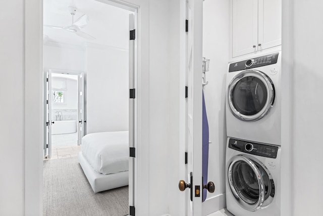 washroom featuring cabinets, stacked washer and dryer, light colored carpet, and ceiling fan