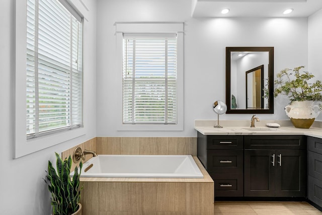 bathroom with plenty of natural light, vanity, and a relaxing tiled tub