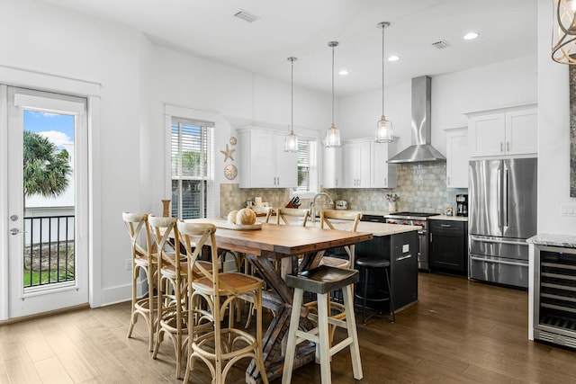 kitchen with wall chimney exhaust hood, a healthy amount of sunlight, white cabinetry, and stainless steel appliances