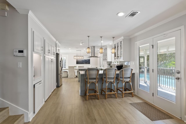 kitchen with white cabinetry, a kitchen breakfast bar, hanging light fixtures, stainless steel fridge, and range hood