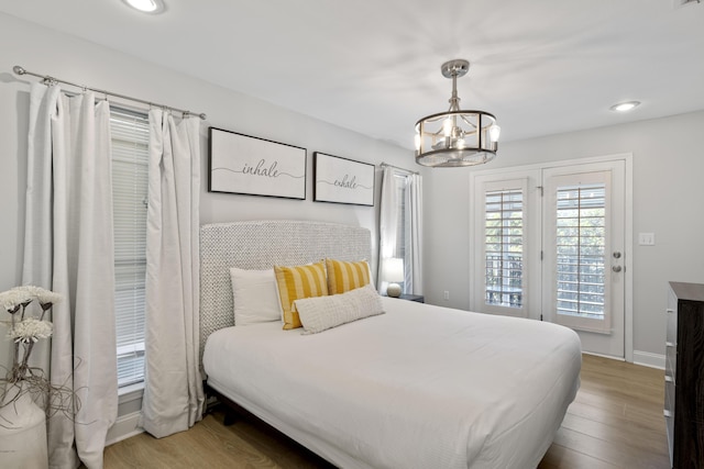 bedroom with wood-type flooring, access to outside, and an inviting chandelier