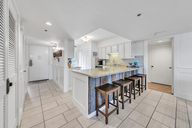 kitchen with light stone counters, white cabinets, sink, decorative backsplash, and a breakfast bar area