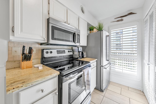 kitchen featuring tasteful backsplash, light stone counters, stainless steel appliances, light tile patterned floors, and white cabinets