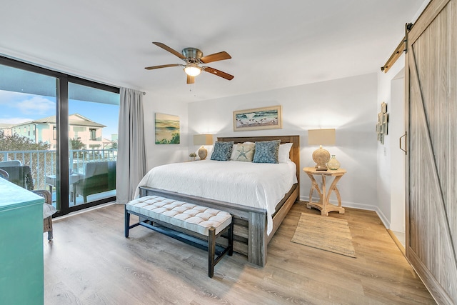 bedroom with access to exterior, light wood-type flooring, a barn door, and ceiling fan