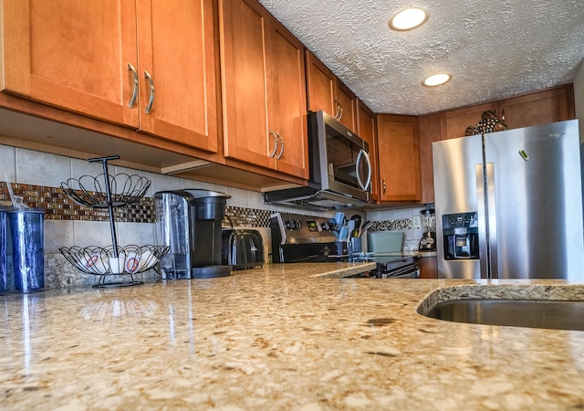 kitchen featuring backsplash, a textured ceiling, light stone counters, and stainless steel appliances